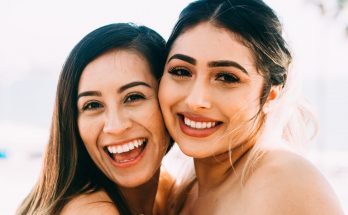 2 smiling women smiling in front of white background